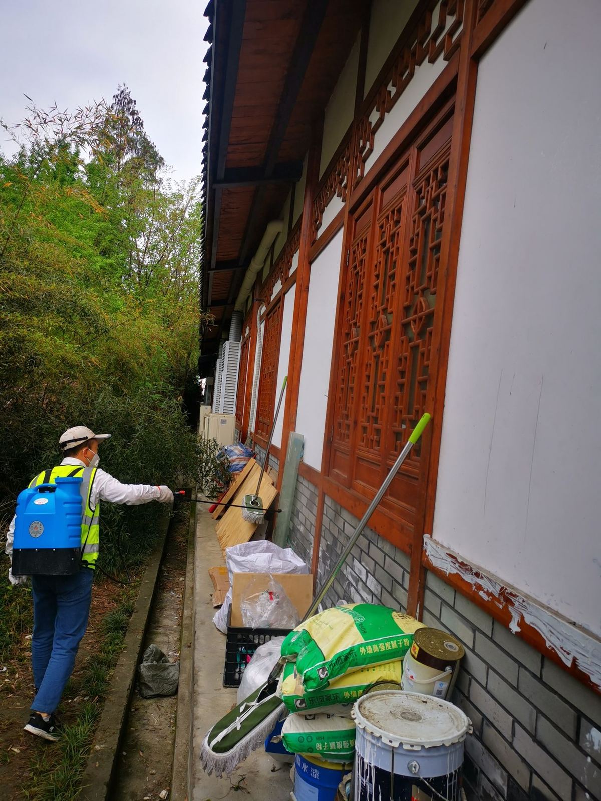 快立克环保四害消杀现场作业实拍：工作人员在建筑墙边，操作绿色设备