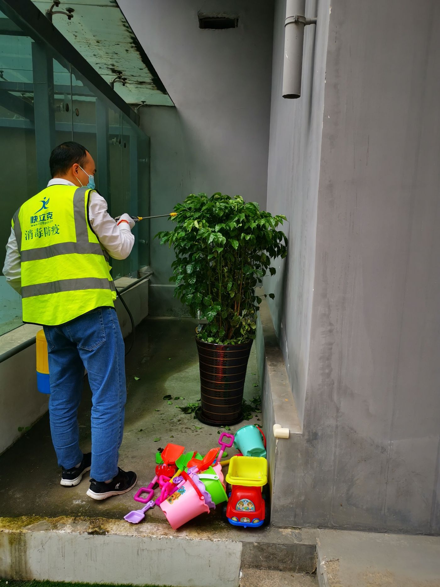 快立克环保四害消杀现场作业实拍：工作人员在建筑门口，附近有植物和物品（可能喷洒）